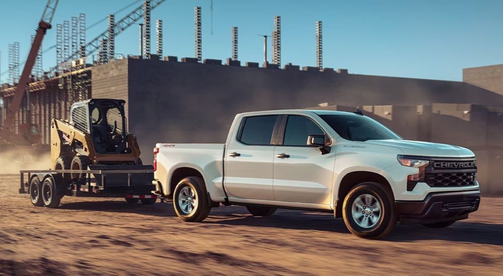 White 2023 Chevy Silverado 1500 towing a construction vehicle