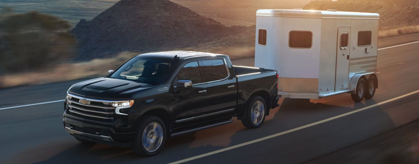 Black 2026 Chevy Silverado 1500 towing a trailor down the road.