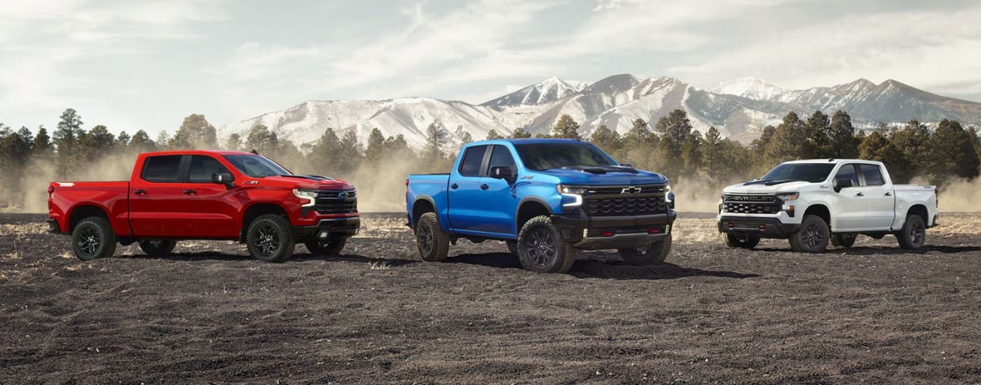 A trio of 2026 Chevy Silverado 1500s in red, white and blue with a mountain in the background.
