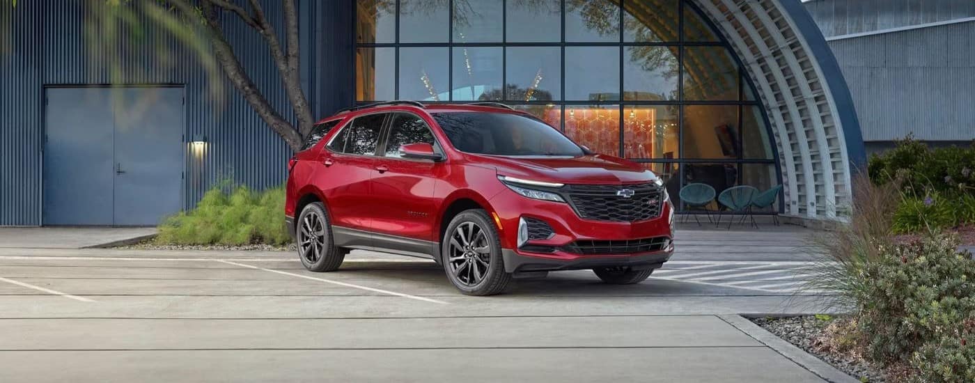 A red 2024 Chevy Equinox RS is parked in front of a modern building.