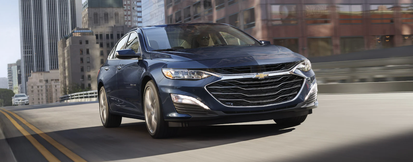 A blue 2022 Chevy Malibu driving in a city.